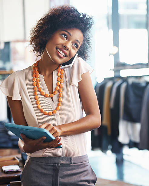 Shot of a busy female clothing boutique owner talking on her phone and holding a tablet